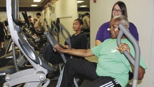 Donna Morris, a personal trainer at the Suffolk Family YMCA, helps Charlotte Cody adjust the settings on the elliptical bicycle.